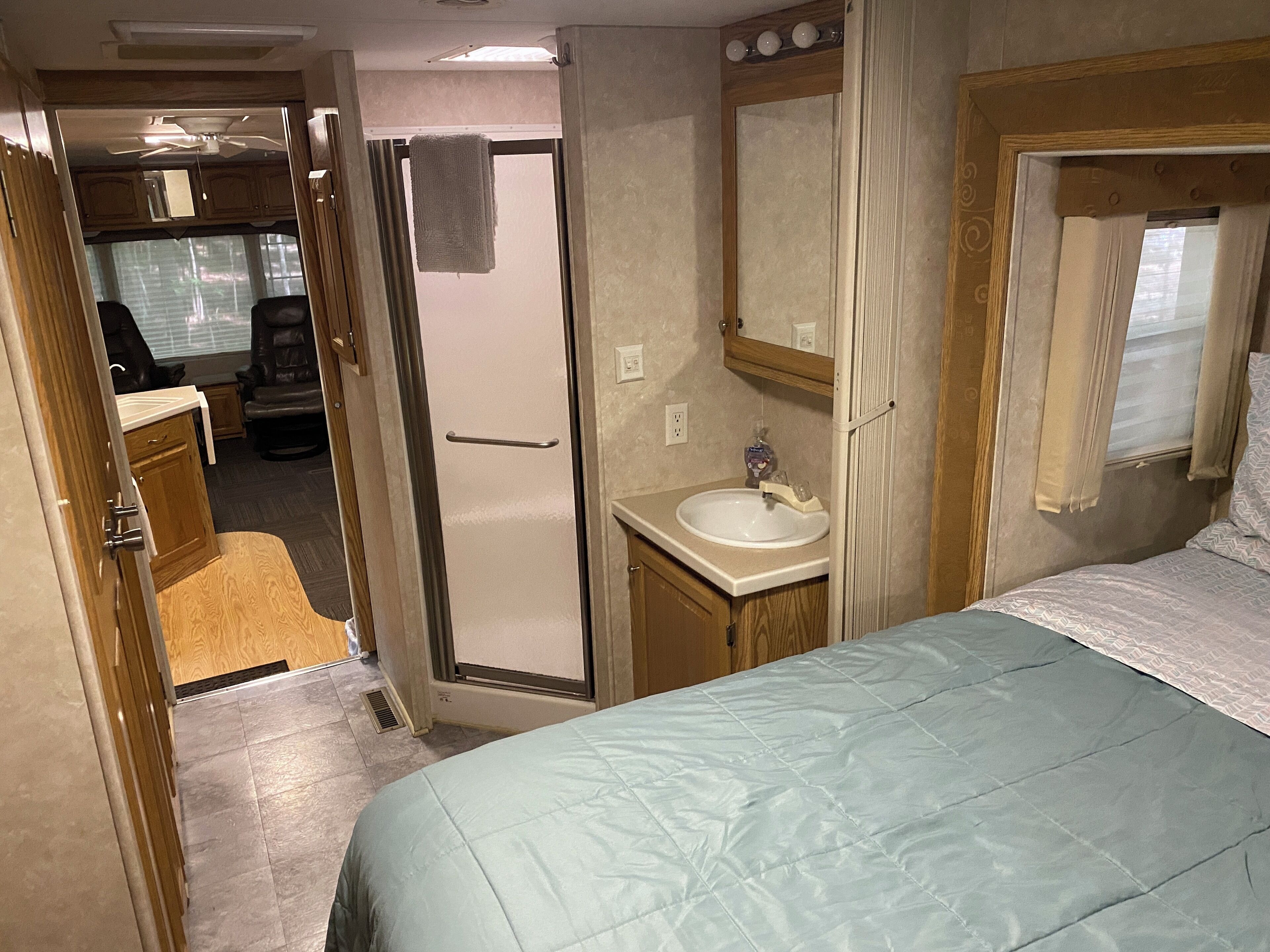 Dormitorio de autocaravana compacto con cama, baño pequeño con lavabo y ducha.