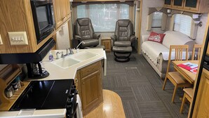 Un intérieur de camping-car compact comprenant un coin cuisine, deux fauteuils inclinables, une petite table et un canapé.