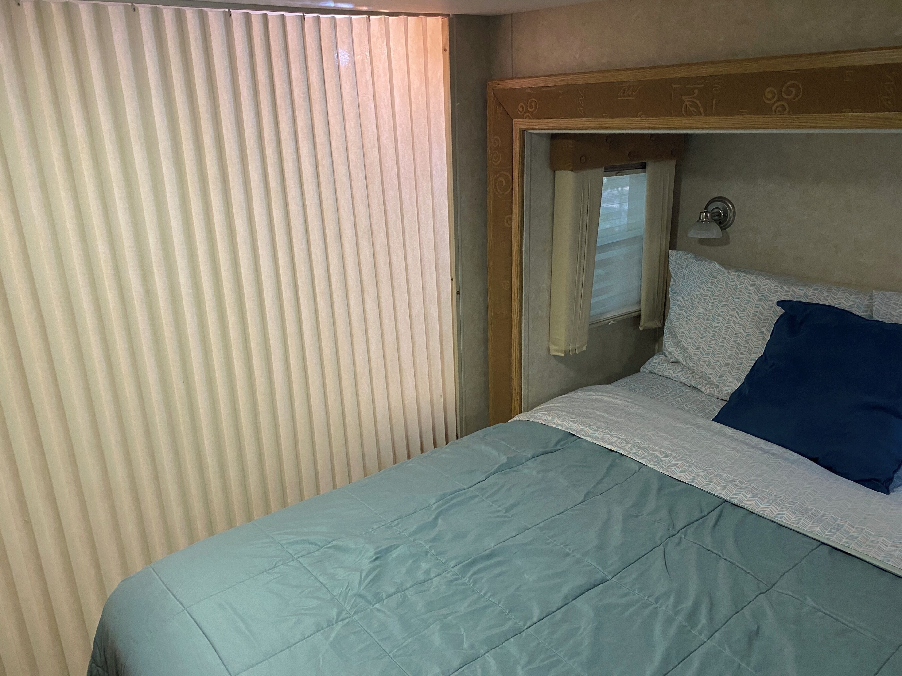 Une chambre avec un lit, une fenêtre avec des rideaux et une tête de lit en bois.