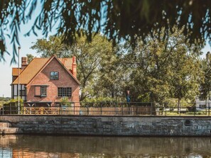 A brick house with a gabled roof, a stone wall, and a wooden fence.