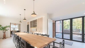 A modern dining area with a long wooden table and black chairs, large windows, and pendant lighting. - Villa Sas by Interhome (Oudenburg)