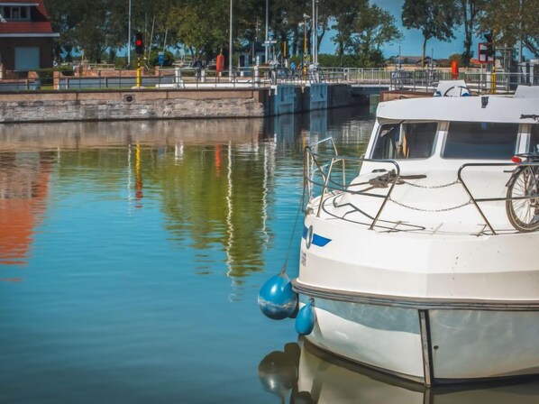 A boat docked at a marina with a calm water surface reflecting nearby structures.