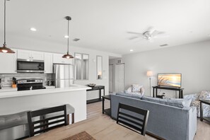 A modern kitchen with a central island, a dining area with a table and chairs, and a living room with a sofa and a TV.