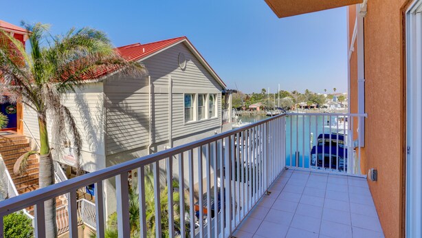 Un balcon donnant sur une marina, une maison avec un toit rouge et un palmier.