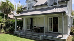 A two-story house with a covered porch, a dining area, and a large window. - Kingfisher Cottage - Russell Cottages Collection (Russell)