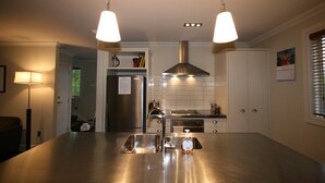 A modern kitchen with stainless steel appliances, a central island, pendant lighting, and a view into the adjacent living area. - Kingfisher Cottage - Russell Cottages Collection (Russell)