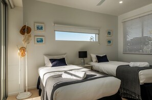 A hotel room with two beds, a standing heater, a window with blinds, and framed pictures on the wall. - Sunshine Coast White House (Castaways Beach)