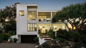 A modern two-story house with a garage, surrounded by landscaped gardens and trees. - Sunshine Coast White House (Castaways Beach)