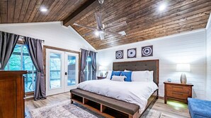 Une chambre avec un grand lit, un plafond en bois et une vue sur l’extérieur, accessible par une porte coulissante.