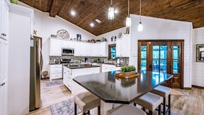 Une cuisine dotée d’un grand îlot central, de meubles blancs et d’un plafond en bois.