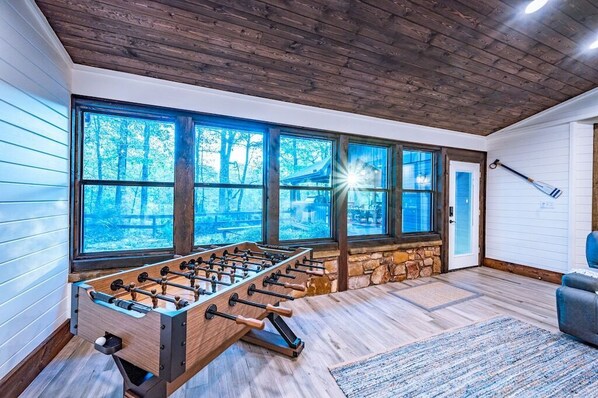 Relax in this spacious room with a high ceiling, featuring a foosball table and comfortable seating area with a sofa and chair.