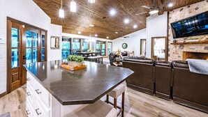 Une cuisine spacieuse avec un grand îlot central, un plafond en bois et une cheminée en pierre.