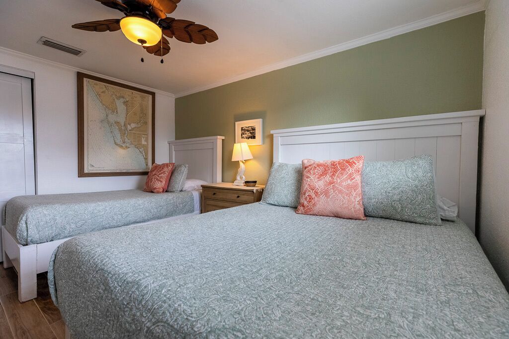 A hotel room with two beds, a ceiling fan, a map on the wall, and a nightstand with a lamp.