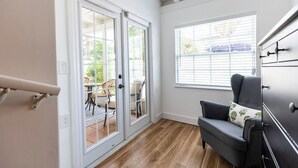 Ein Zimmer mit einer Schiebeglastür, die zu einer Terrasse im Freien führt, einem dunkelgrauen Sofa und einem Fenster mit Jalousien.