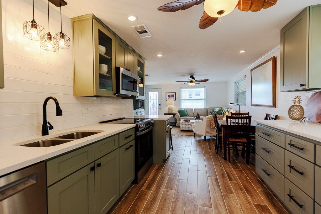 Una cocina moderna con piso de madera, gabinetes verdes y una isla central.