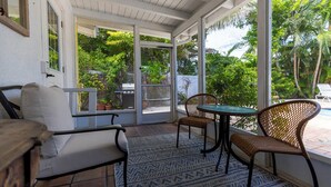 Eine überdachte Terrasse mit einer Couch, zwei Korbstühlen und einem Tisch.