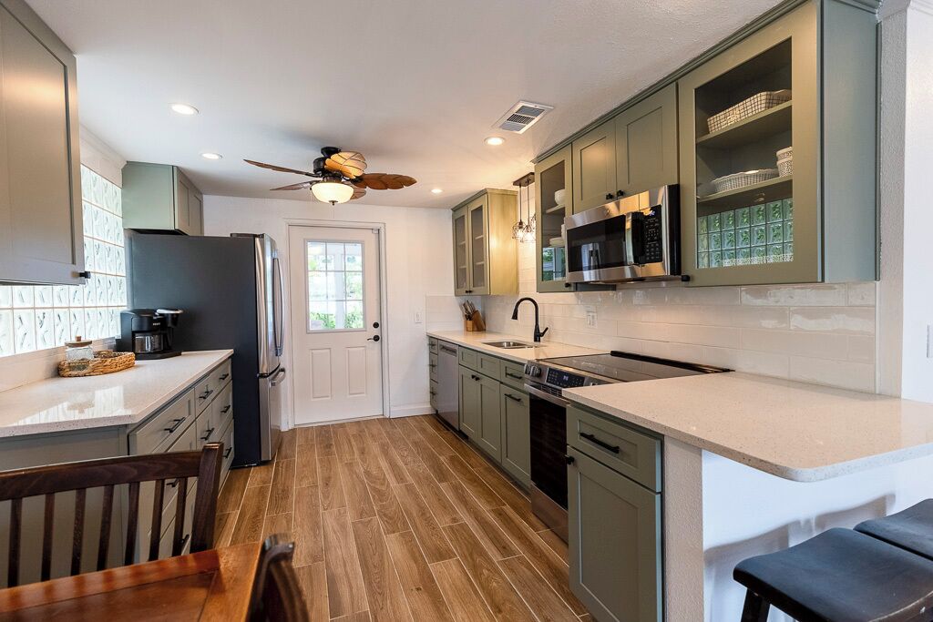 Una cocina moderna con suelo de madera, armarios verdes y horno empotrado, además de un ventilador de techo.