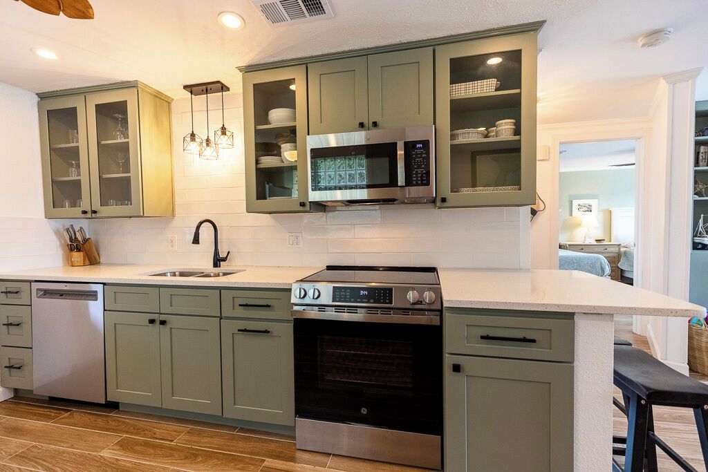A kitchen with green cabinets, a microwave, an oven, and a dishwasher.