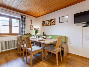 A dining area with a wooden table, chairs, a bench, a radiator, a window with curtains, a crucifix, and a framed picture on the wall. - Spacious apartment with a balcony (Wagrain)