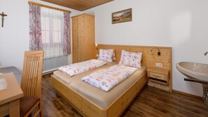 Un dormitorio con una cama de madera, una mesita de noche, un armario de madera, una ventana con cortinas, un radiador y un cuadro en la pared.