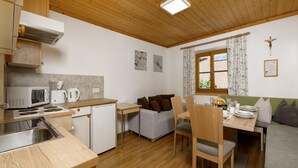 Cocina compacta con microondas, cafetera y lavamanos. Hay una zona de comedor con una mesa dispuesta para dos personas, y un sofá al fondo.