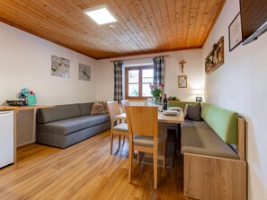 A cozy living space with a wooden ceiling, a dining table with chairs, a sofa, and a small kitchen area. - Spacious apartment with a balcony (Wagrain)
