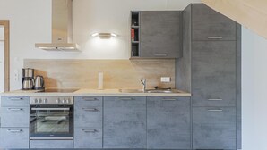 Una cocina moderna con armarios grises, horno empotrado, cafetera y lavamanos.