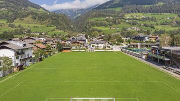 Un terrain de football avec des buts, entouré de bâtiments résidentiels et avec des montagnes en arrière-plan.