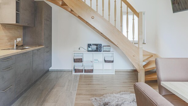 Una cocina moderna con armarios grises, una escalera de madera y un mueble de almacenaje blanco con cestas.