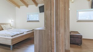 Un dormitorio con cama, un banco y televisor montado en la pared.