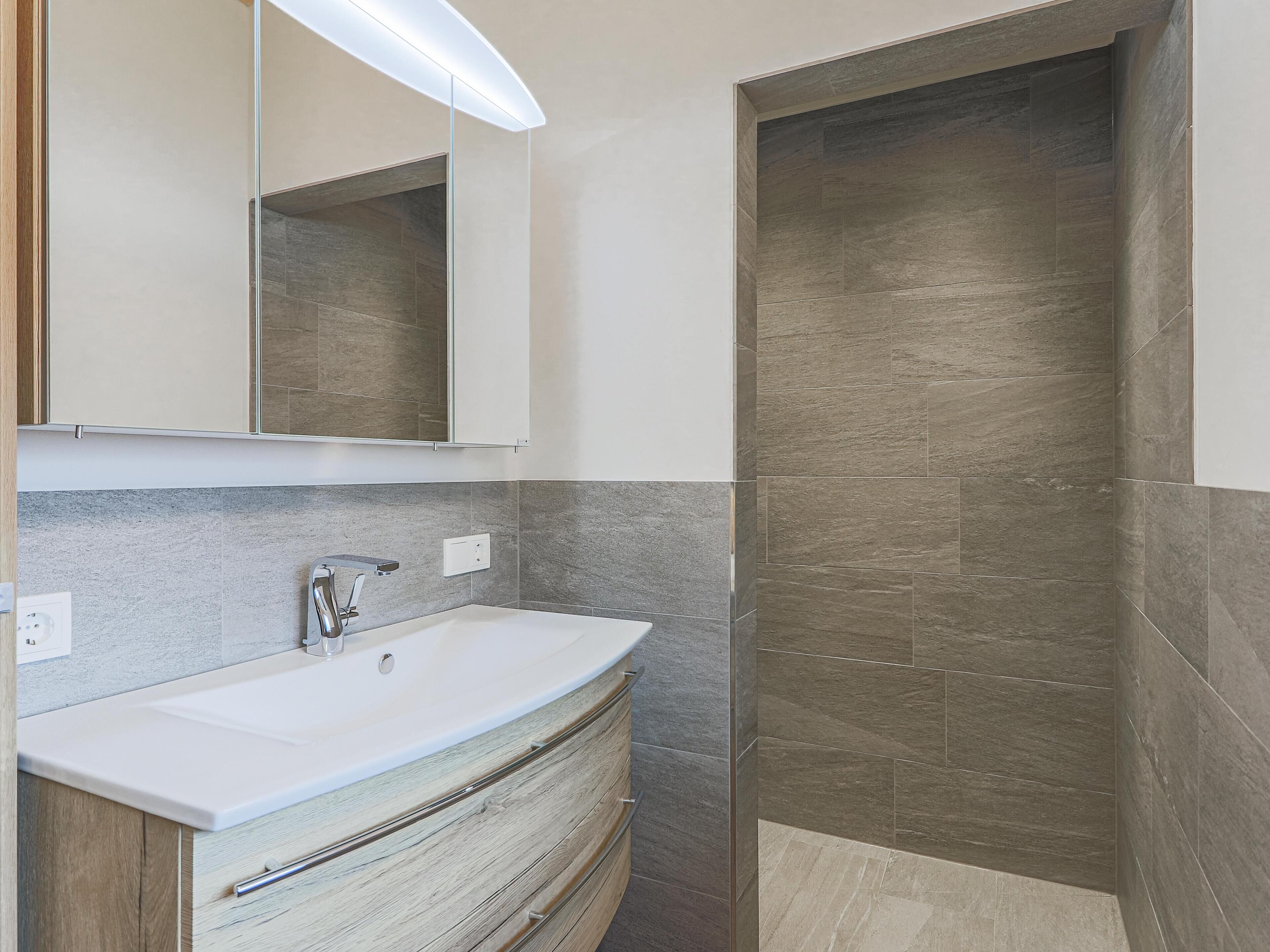 Une salle de bain moderne avec un lavabo blanc, un meuble-lavabo en bois et une cabine de douche en verre.