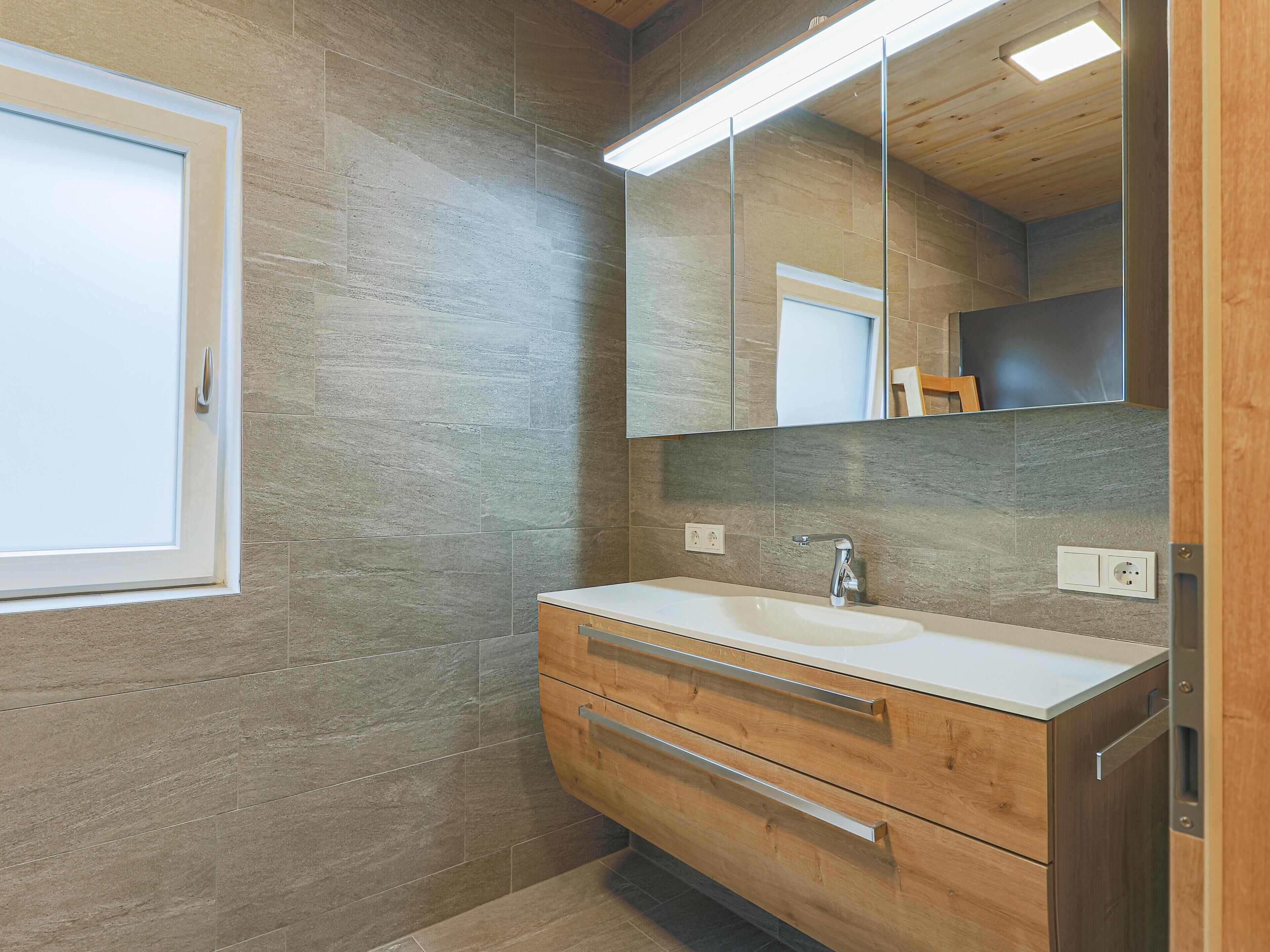 A bathroom with a wooden vanity, a white sink, and a large mirror.