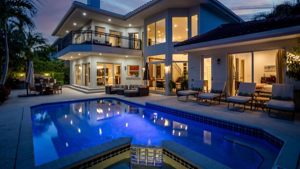 Une maison à deux étages avec une piscine, un espace salon extérieur et un balcon.