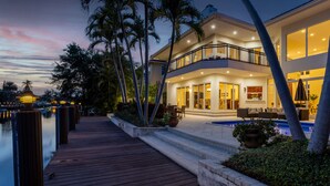 Une propriété située au bord de l’eau, dotée d’une terrasse en bois, d’une piscine et d’une maison à deux étages avec un balcon.