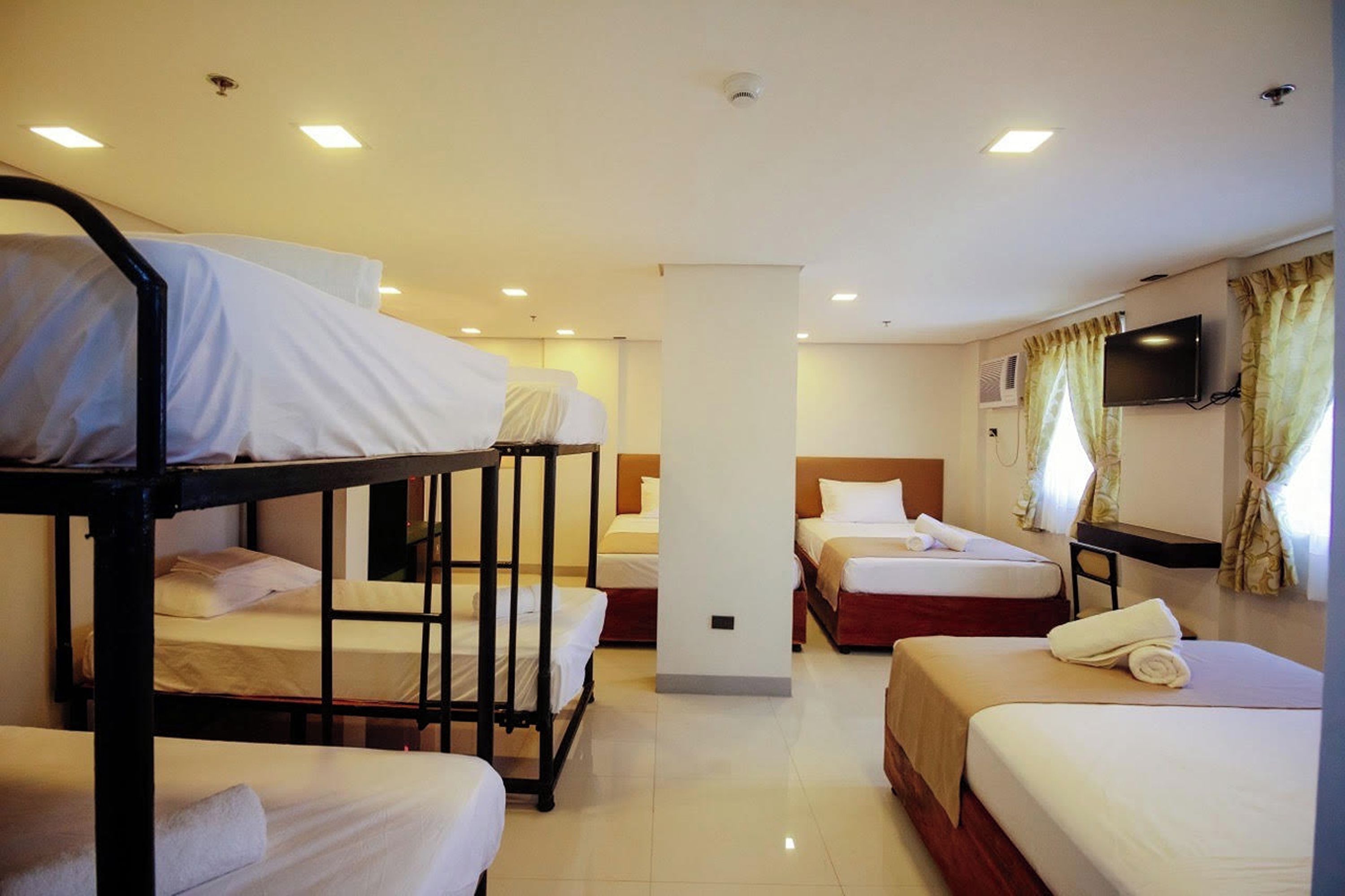 A hotel room with bunk beds, a flat-screen TV, and a large window with curtains.