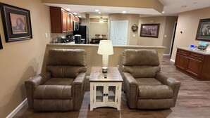 Una sala de estar con dos sillones de cuero, una mesita y una cocina al fondo.