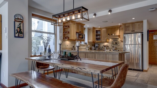 Una cocina moderna con armarios de madera, un refrigerador de acero inoxidable y una zona de comedor con mesa y sillas de madera.