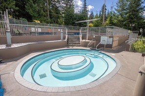 A circular pool with a central water feature, surrounded by a concrete deck and metal railings. - Woodrun 208 - Ski in Ski out, Common Area Hot Tub & Pool, Gas Fireplace, BBQ (Whistler)