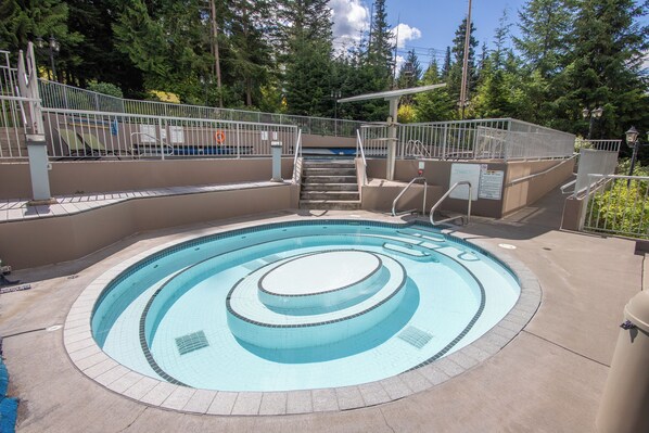 A circular pool with a central water feature, surrounded by a concrete deck and metal railings.