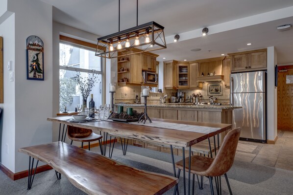 A modern kitchen with wooden cabinets, a stainless steel refrigerator, and a dining area with a wooden table and chairs. - Woodrun 208 - Ski in Ski out, Common Area Hot Tub & Pool, Gas Fireplace, BBQ (Whistler)