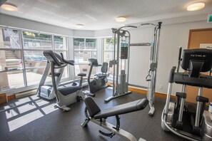 A gym with various exercise equipment, large windows, and a view of outdoor stairs.