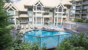 Un hotel de varios pisos con piscina rodeada por una cerca, balcones y zonas de estar al aire libre.