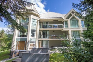 A multi-story residential building with balconies, large windows, and a stone foundation. - Woodrun 208 - Ski in Ski out, Common Area Hot Tub & Pool, Gas Fireplace, BBQ (Whistler)