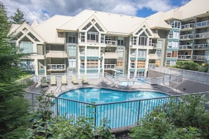 A multi-story hotel with a swimming pool surrounded by a fence, balconies, and outdoor seating areas. - Woodrun 208 - Ski in Ski out, Common Area Hot Tub & Pool, Gas Fireplace, BBQ (Whistler)