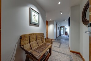 A hallway with a wooden bench, a framed picture on the wall, and a door with a round mirror. - Woodrun 208 - Ski in Ski out, Common Area Hot Tub & Pool, Gas Fireplace, BBQ (Whistler)