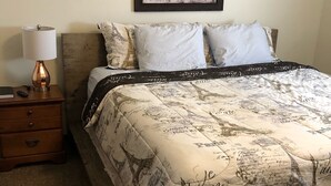 A bedroom with a bed featuring a Paris-themed duvet, a nightstand with a lamp, and a framed picture of horses on the wall.