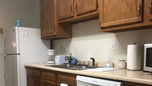 A kitchen with wooden cabinets, a white refrigerator, a dishwasher, and a countertop with a kettle and a coffee maker.