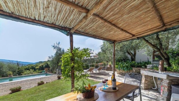 An outdoor patio with a wooden table, chairs, and a bottle of wine. - Vacation home Olivo by Interhome (Castellina in Chianti)