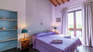 A bedroom with a bed, two bedside tables, a shelf unit, a window with curtains, and a wooden ceiling. - Vacation home Olivo by Interhome (Castellina in Chianti)