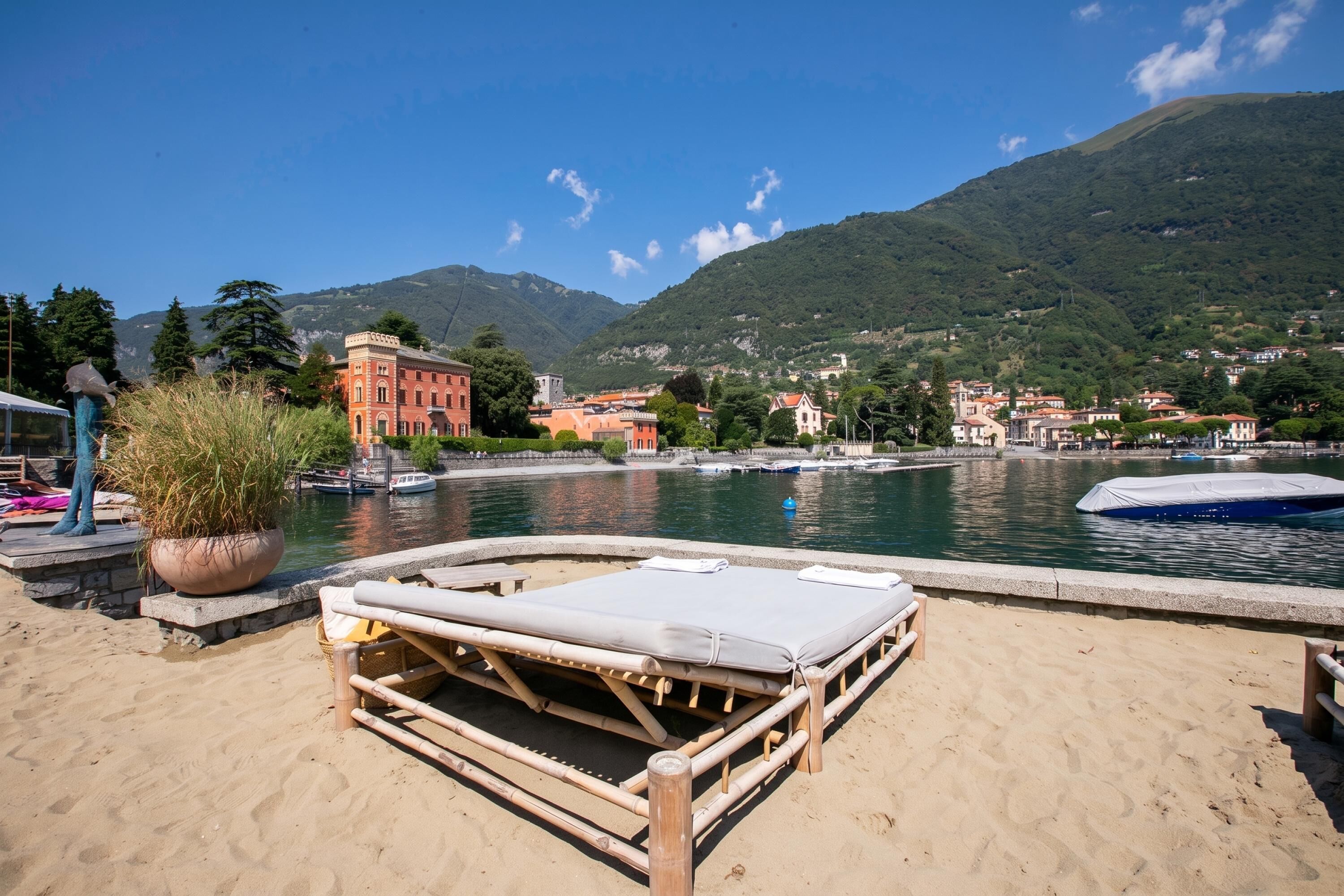 A beach with a lounge chair, a potted plant, and a water body with boats.